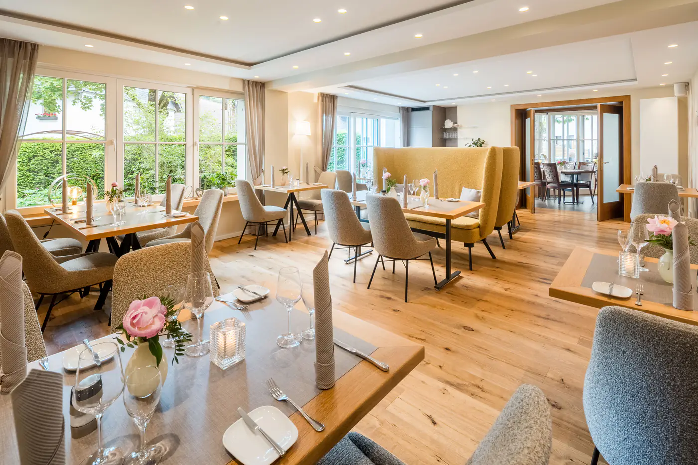 Eingedeckte Tische im Restaurant mit hellem Holzboden und Blick ins Grüne