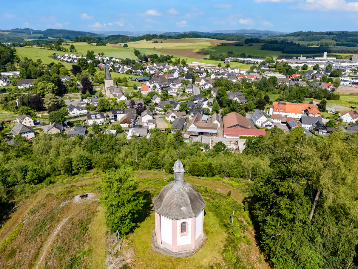 Die Rehbergkapelle auf ihrem bewaldeten Hügel, dahinter das Dorf Stockum