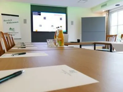 Tischreihe mit bereitgelegten Blöcken und Stiften, Blick auf Leinwand und Willkommensaufsteller
