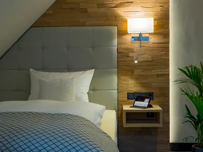 Bett im Heysmer Landhaus vor einer Holzwand mit warmem Leselicht